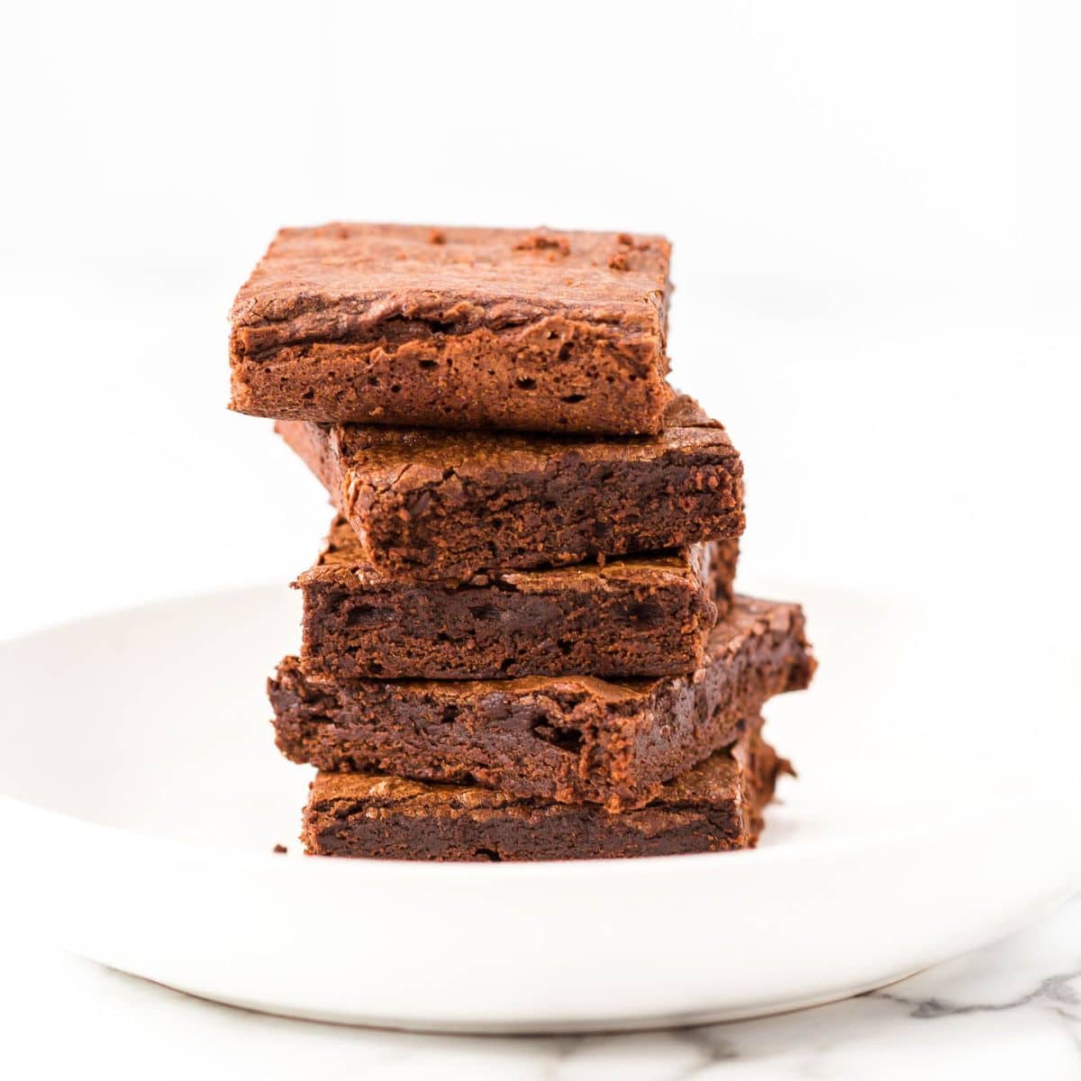 A stack of four Triple Chocolate Brownies arranged on a white plate against a white background.
