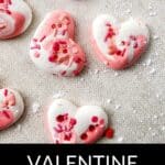 Heart-shaped pink and white meringue cookies with red and pink sprinkles on a textured surface; text reads "Valentine Meringue Cookies"—a delightful treat perfect for sharing your love of meringue cookies.