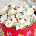 Chocolate Covered Popcorn topped with red, green, and white sprinkles comes in a festive red holiday tin adorned with snowflakes and Christmas trees.
