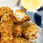 Air Fryer Fish Sticks garnished with parsley, served with a side of lemon and a dipping sauce.
