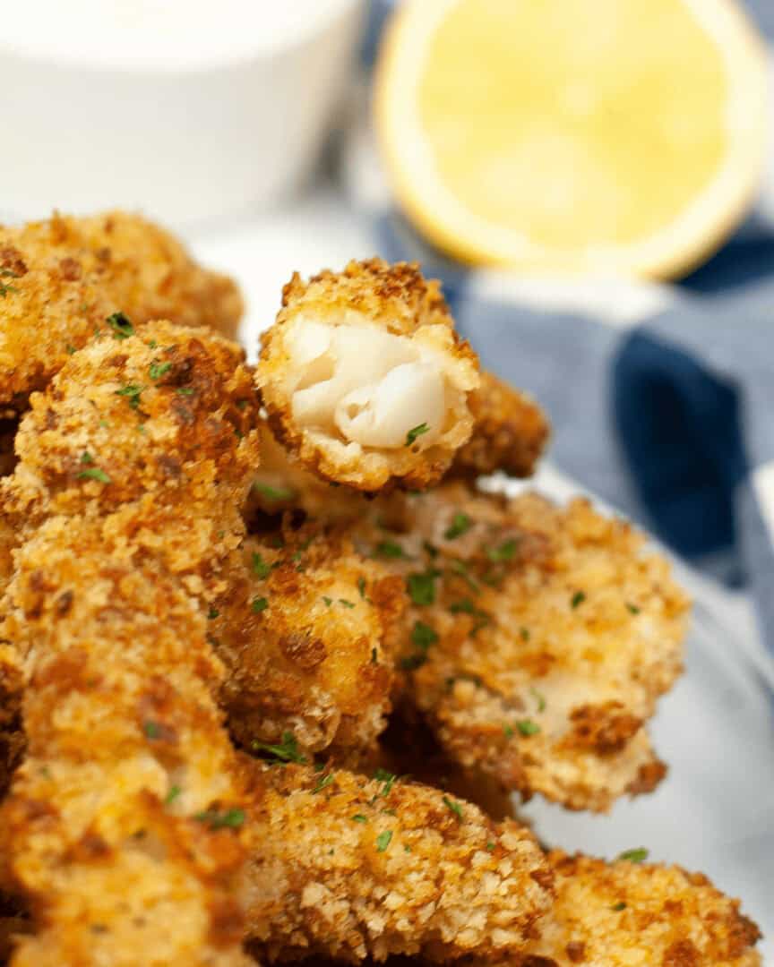 Air Fryer Fish Sticks garnished with parsley, served with a side of lemon and a dipping sauce.