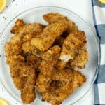 A plate of crispy, air fryer fish sticks garnished with parsley, accompanied by lemon wedges and a striped napkin.