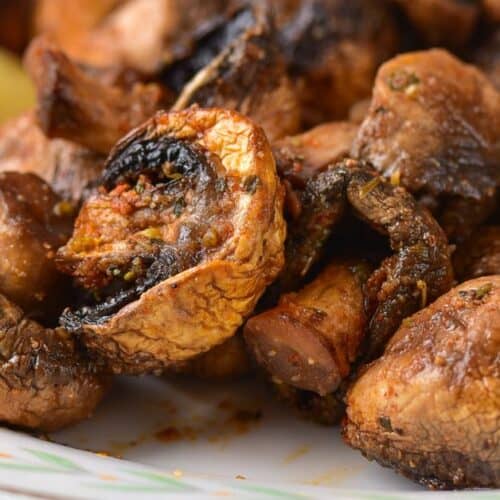 Air Fryer Mushrooms roasted with herbs on a white plate, served with lemon wedges.