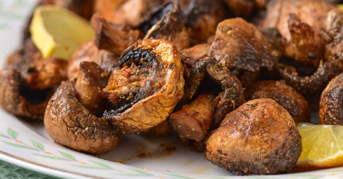 Air Fryer Mushrooms roasted with herbs on a white plate, served with lemon wedges.