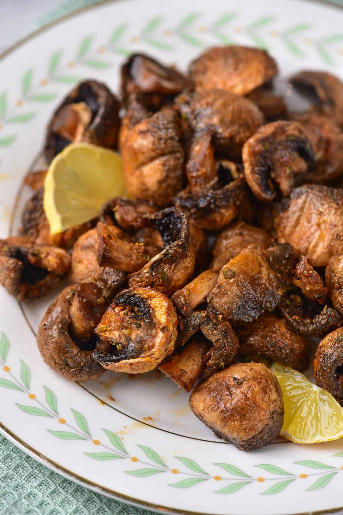 A plate of Air Fryer Mushrooms garnished with lemon wedges, served on a decorative white plate with a green and gold border.