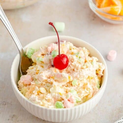 A white bowl of ambrosia salad with a cherry on top.