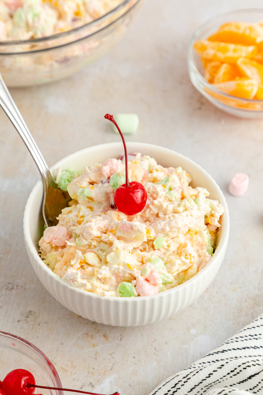 A bowl of the Ambrosia Salad with Cool Whip with a cherry on top.