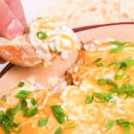 A person dipping a piece of bread into a bowl of cowboy crack dip.