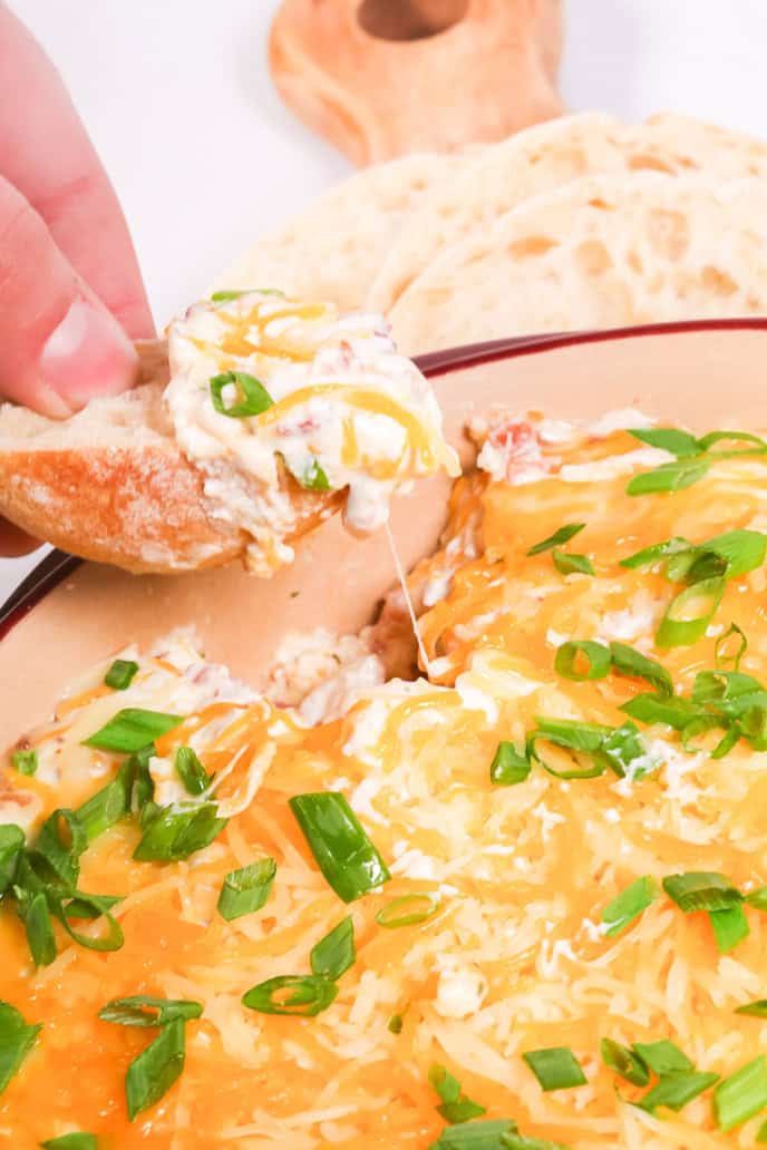 A person dipping a piece of bread into a bowl of cowboy crack dip.