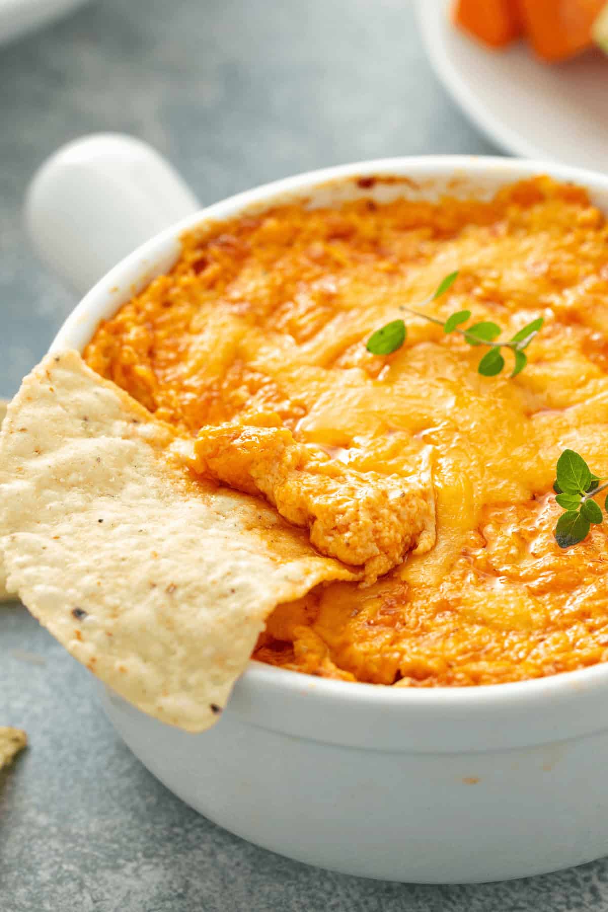 A bowl of cheesy treat with a tortilla chip inserted, garnished with a few fresh herbs.