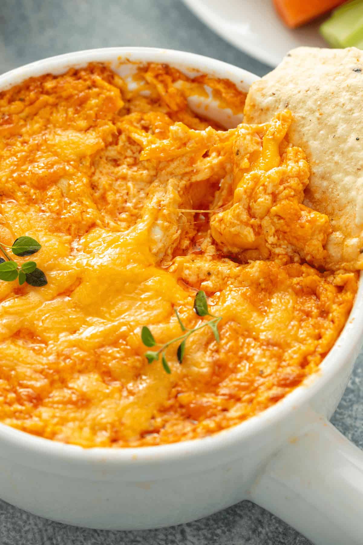  Dip in a white bowl, topped with melted cheese and garnished with thyme, with a cracker dipped into the mixture.