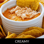 A ramekin of creamy baked Buffalo Chicken Wing Dip is topped with shredded chicken and surrounded by a crunchy halo of tortilla chips.