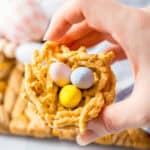 A hand holding homemade bird’s nest cookies with colorful candy eggs.