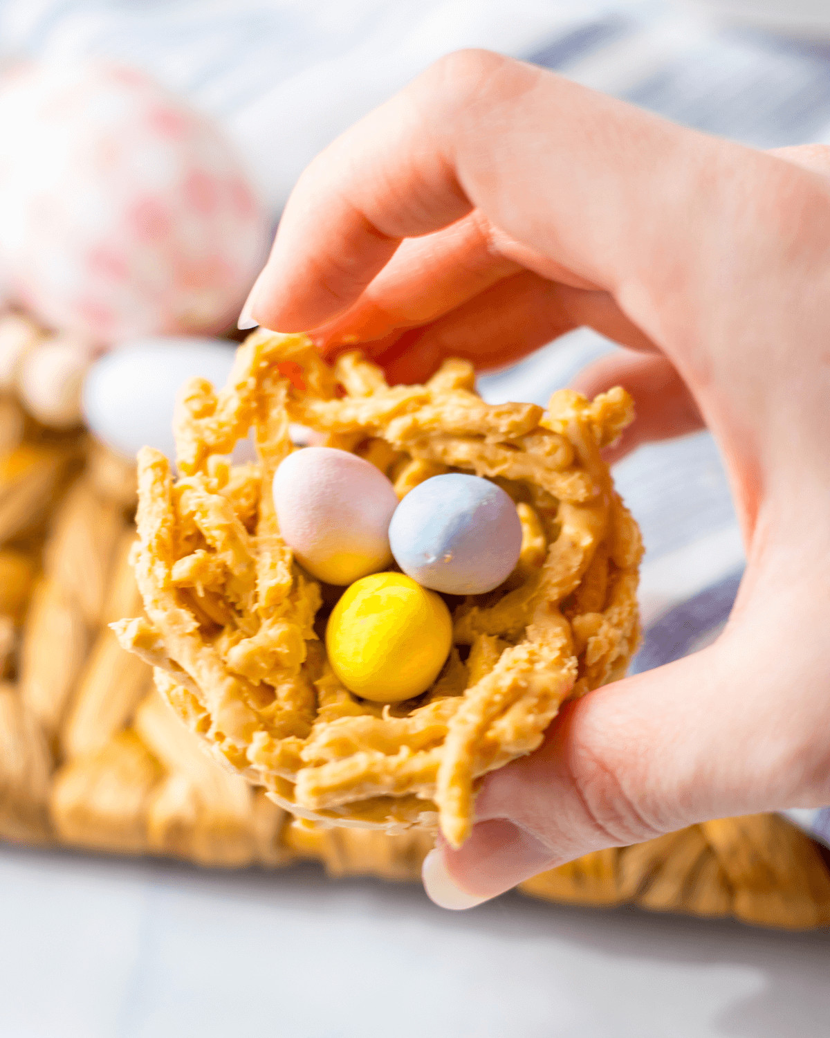 A hand holding homemade bird’s nest cookies with colorful candy eggs.