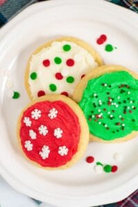 Three sugar cookies on a white plate, each decorated with red, green, or white buttercream frosting for cookies and festive sprinkles.