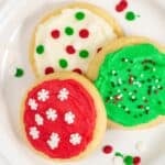 Three round sugar cookies on a white plate, topped with vibrant red, white, and green buttercream frosting for cookies, and decorated with festive sprinkles.