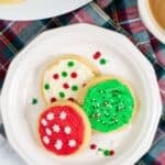 A white plate with three decorated with festive sprinkles, beside a cup of coffee.