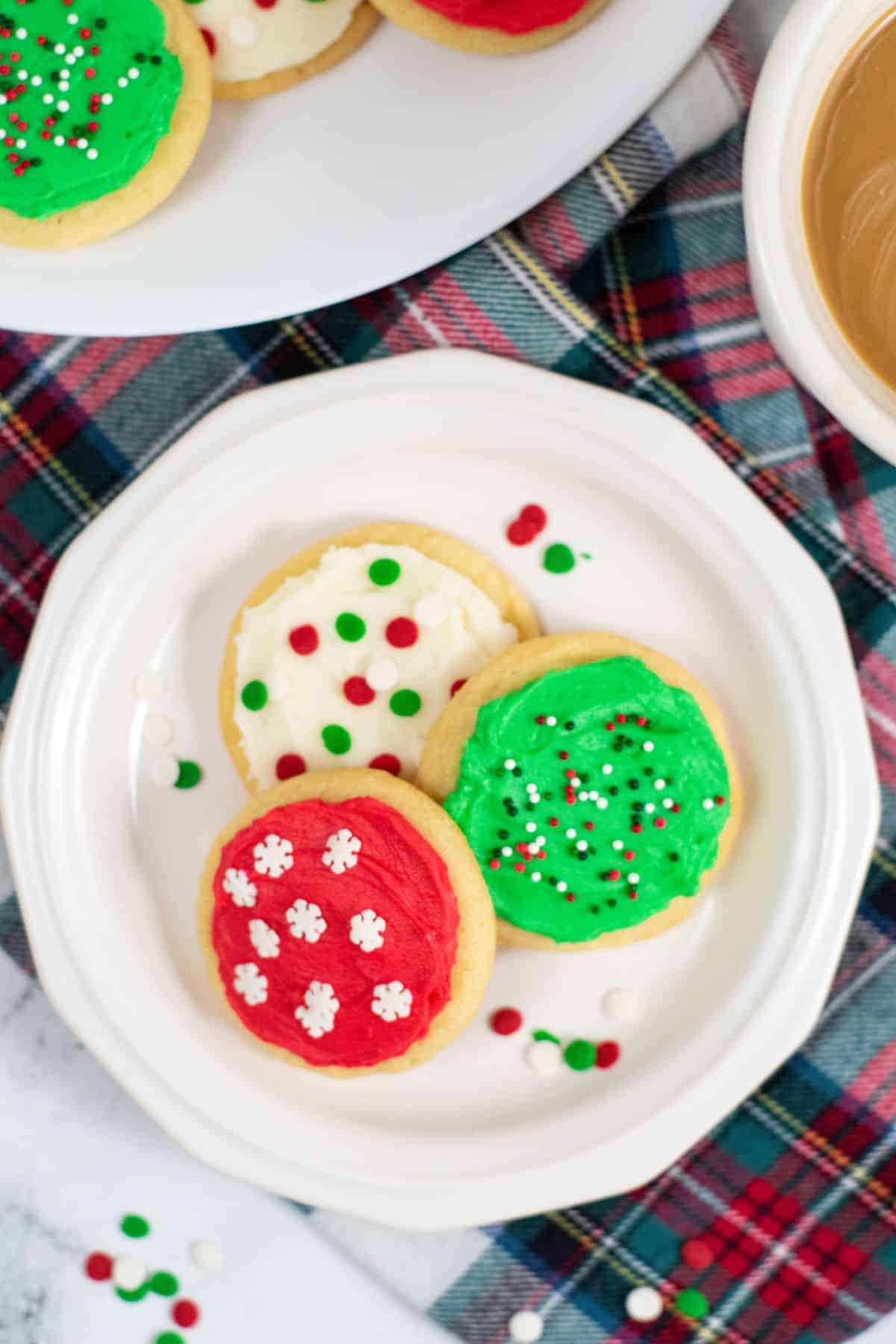 A white plate with three decorated with festive sprinkles, beside a cup of coffee.