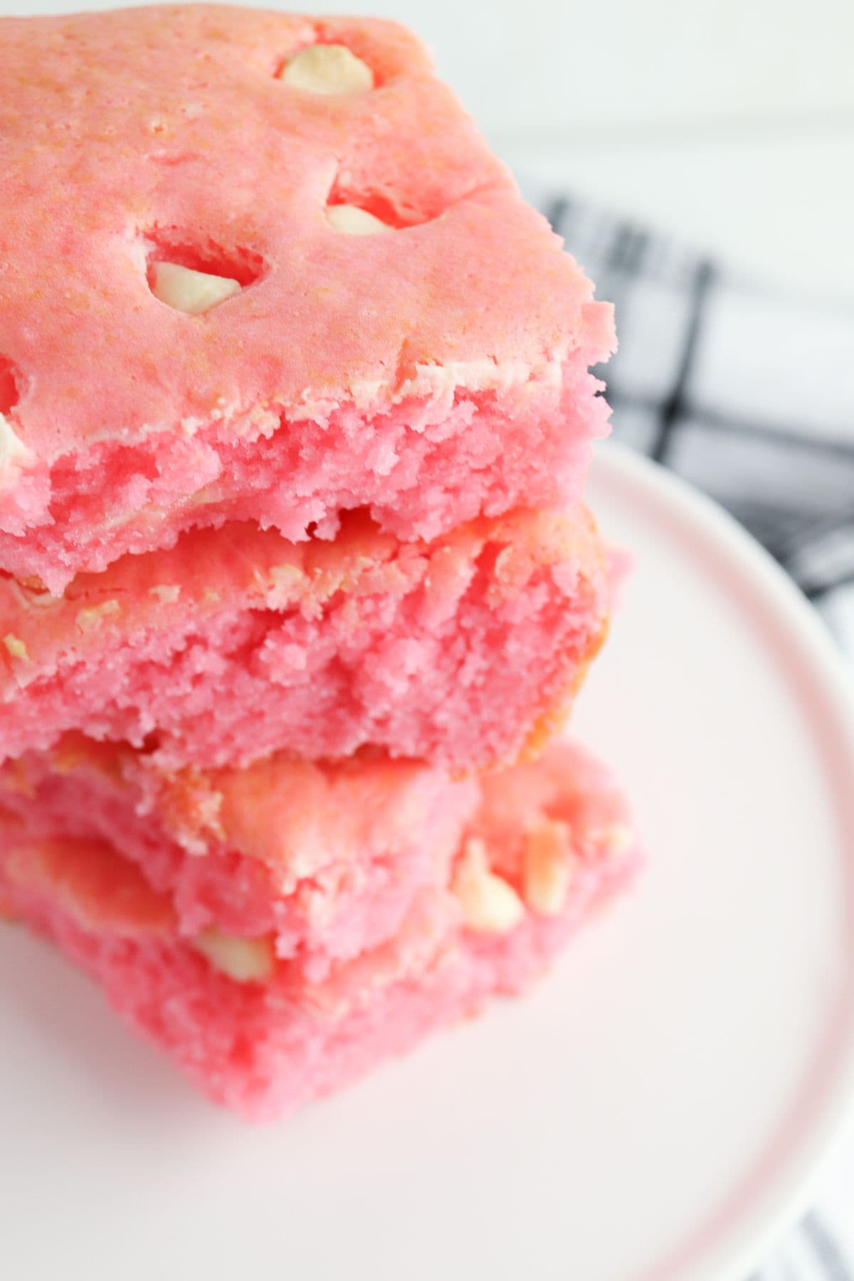 Three stacked pink cake mix strawberry brownies with white chocolate chips on a white plate, shown in close-up.
