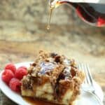 A plate with two pieces topped with syrup, served with fresh raspberries and a fork. Syrup is being poured from a glass pitcher.