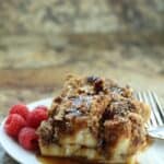A plate with two pieces of casserole drizzled with syrup and topped with pecans, served alongside fresh raspberries and a fork.