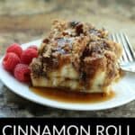 Two pieces of delicious Cinnamon Roll French Toast are served on a white plate with fresh raspberries, forks, and syrup atop a brown countertop. Text reads "Cinnamon Roll French Toast Bake.