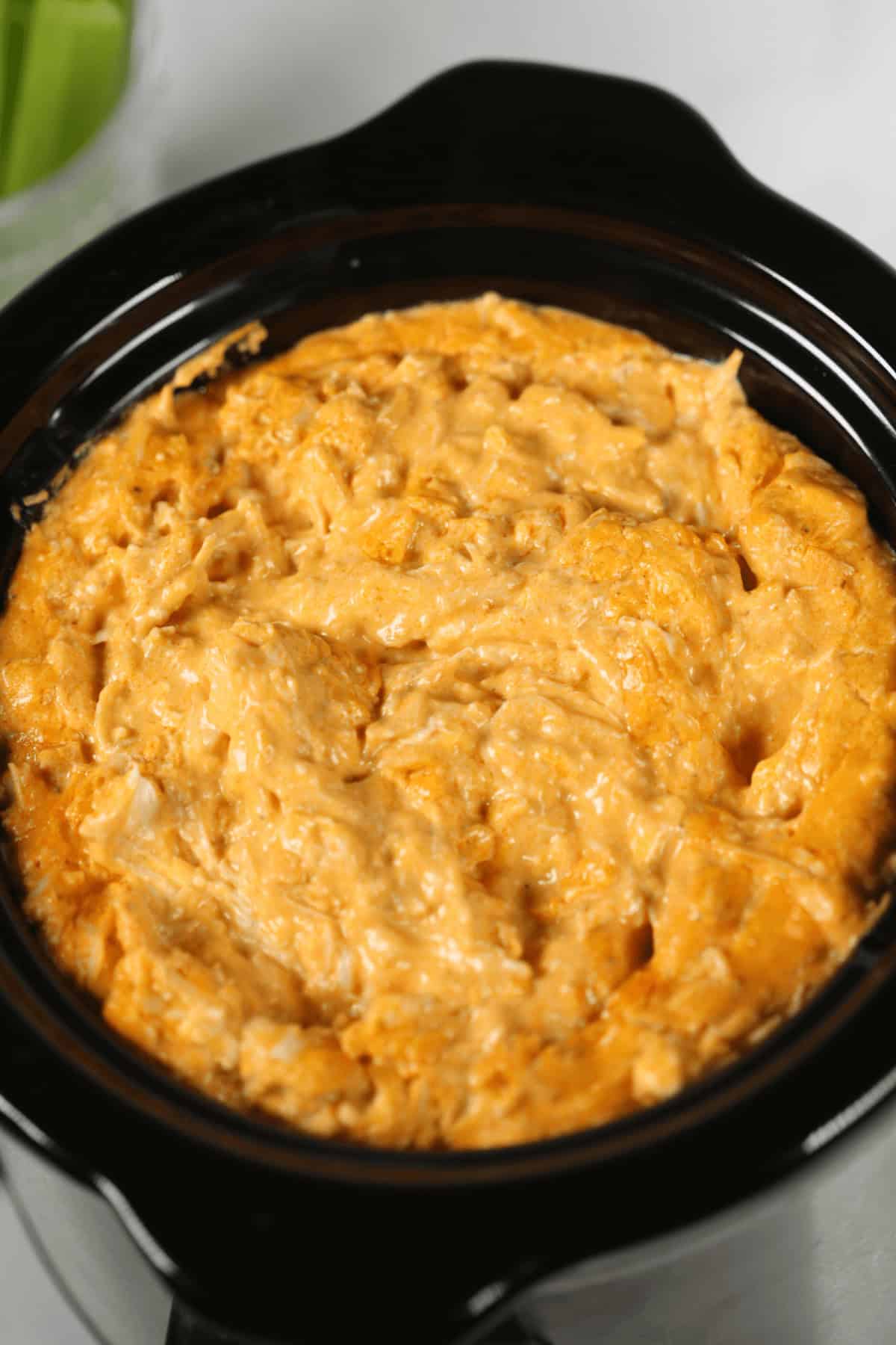 Close-up of a creamy, orange-yellow Crock Pot Buffalo Chicken Dip in a black slow cooker.