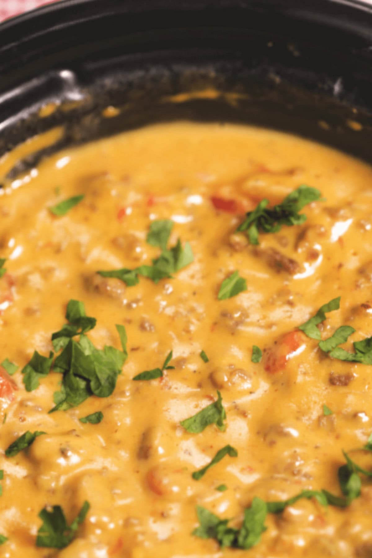 Close-up of creamy Crock Pot Cheeseburger Dip featuring ground meat, chopped tomatoes, and topped with fresh cilantro, all elegantly served in a black bowl.