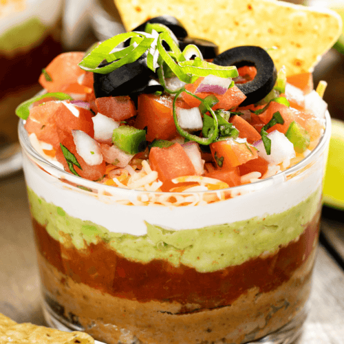 Experience the ultimate 5 Layer Dip in a glass, complete with refried beans, guacamole, sour cream, shredded cheese, salsa, diced tomatoes, black olives, and green onions—crowned with a crispy tortilla chip for the perfect bite.