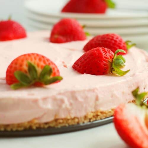 A close-up of the dessert with a crumbly base, topped with whole strawberries, and plates in the background.