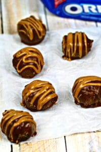 Six chocolate truffles drizzled with caramel are arranged on parchment paper, reminiscent of decadent Peanut Butter Bon Bons, with an Oreo cookie package partially visible in the background.