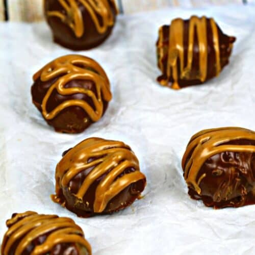 Six chocolate truffles drizzled with caramel are arranged on parchment paper, reminiscent of decadent Peanut Butter Bon Bons, with an Oreo cookie package partially visible in the background.