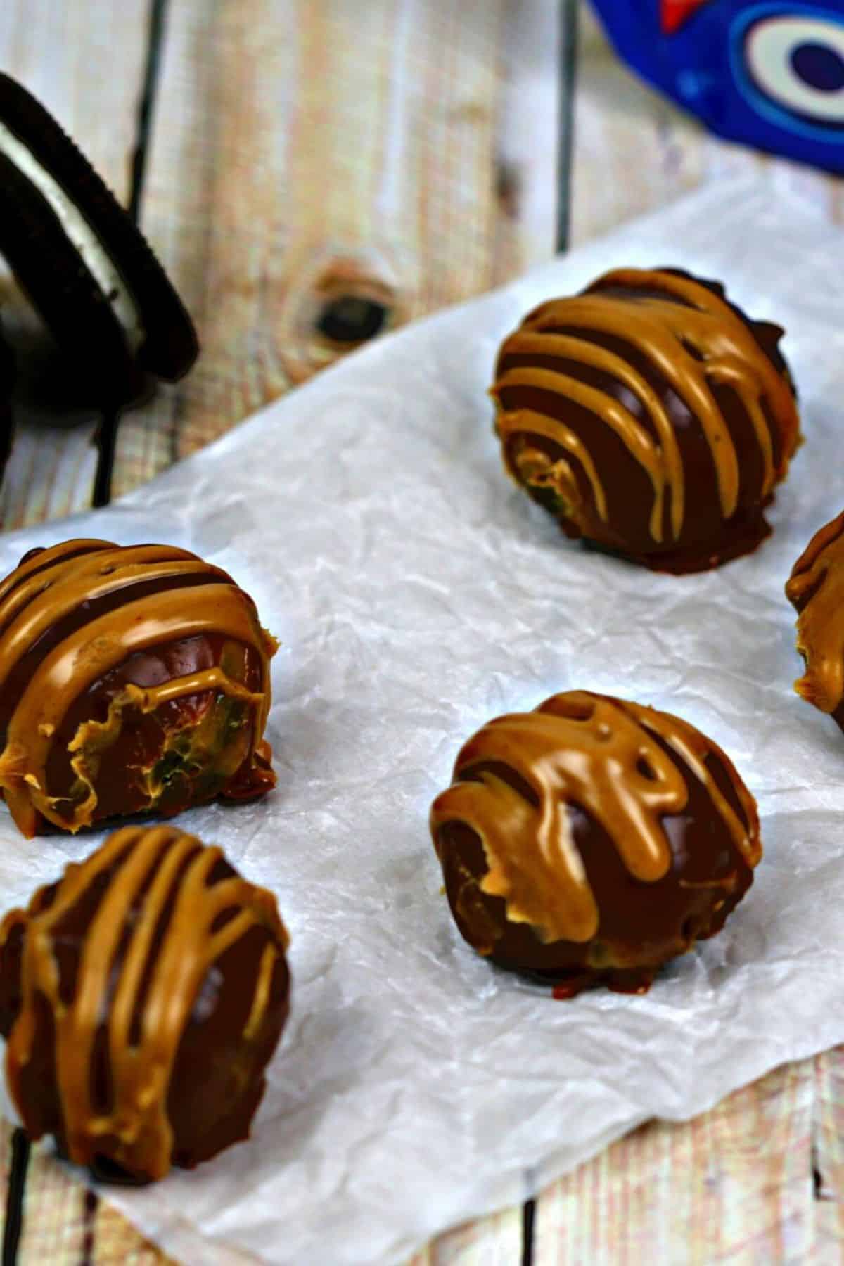 Five round treats with a caramel-colored drizzle rest on crumpled white parchment paper; a partially visible cookie is in the background.