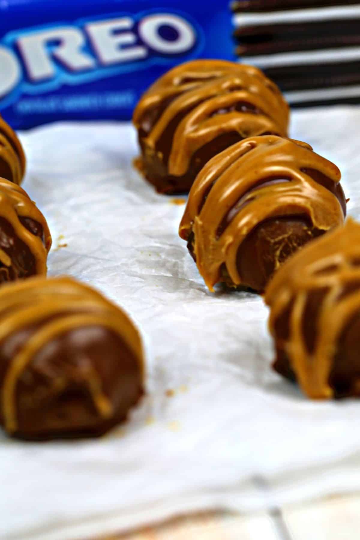 Truffles with a drizzle of peanut butter sit on parchment paper, with an Oreo cookie package partially visible in the background.