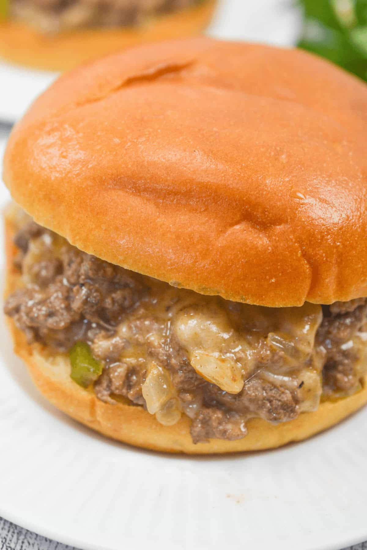 Close-up of a Philly Cheese Steak Sloppy Joe sandwich with savory beef mixture and onions, served on a white plate.