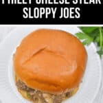 A delicious Philly Cheese Steak Sloppy Joe rests on a white plate, its savory goodness invitingly displayed atop a light wooden surface.