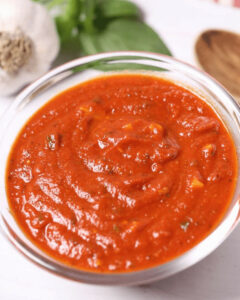 A bowl of fresh San Marzano tomato sauce garnished with basil leaves, alongside garlic and spices.