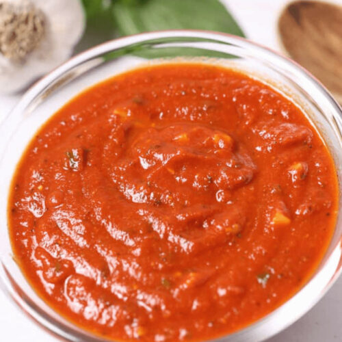 A bowl of fresh San Marzano tomato sauce garnished with basil leaves, alongside garlic and spices.