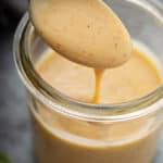 A spoonful of creamy yellow sauce with specks is lifted from a glass jar half-filled with spicy honey mustard goodness.