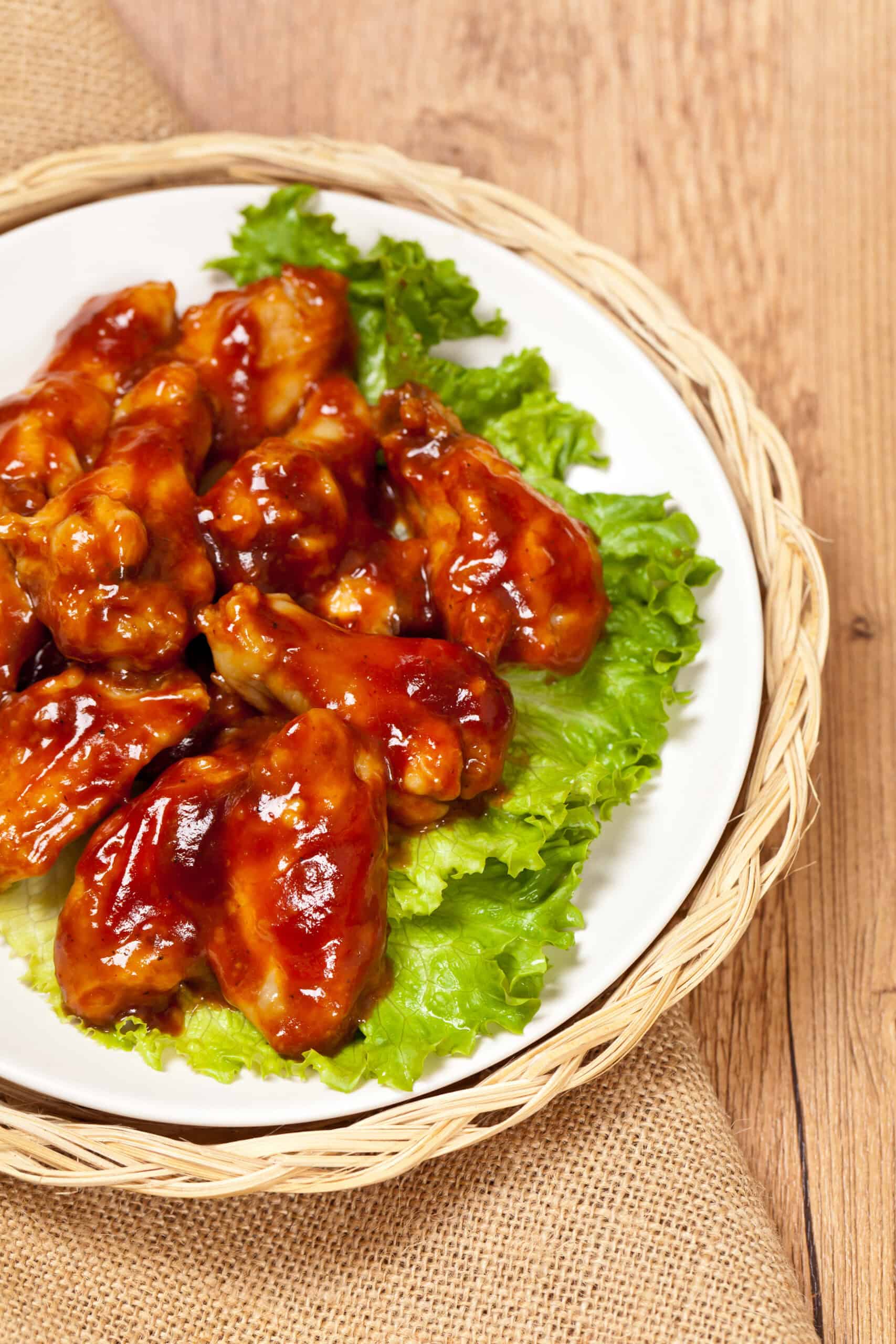 A white plate with the sweet and spicy wings on top of a bed of lettuce.