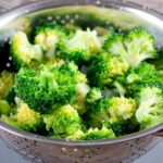 A colander full of cooked broccoli.