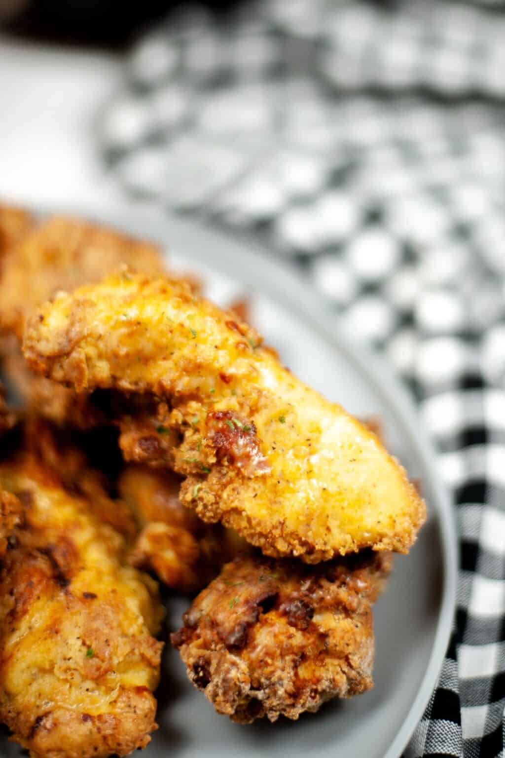Close-up of crispy Air Fryer Chicken Strips on a gray plate, with a black and white checkered cloth in the background.