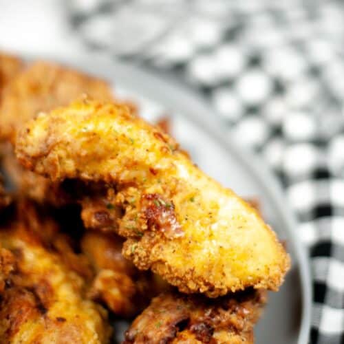 Close-up of crispy Air Fryer Chicken Strips on a gray plate, with a black and white checkered cloth in the background.