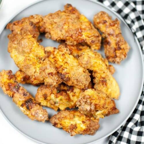 A plate of crispy Air Fryer Chicken Strips is placed next to a black and white checkered cloth, with a bowl of green beans partly visible in the corner.