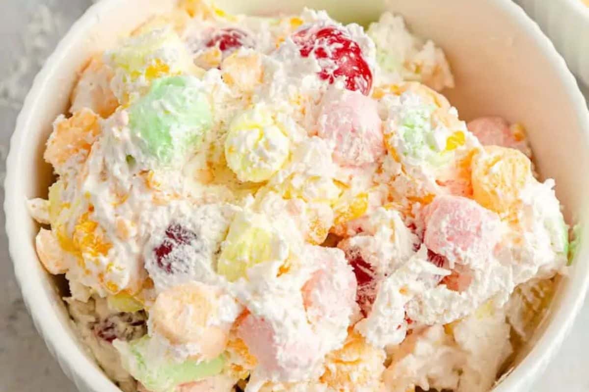 A bowl of pastel-colored ambrosia salad with whipped cream, cherries, and mixed fruit pieces makes for delightful Easter treats for kids.