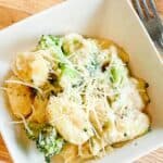 A square white bowl with creamy gnocchi alfredo with broccoli.