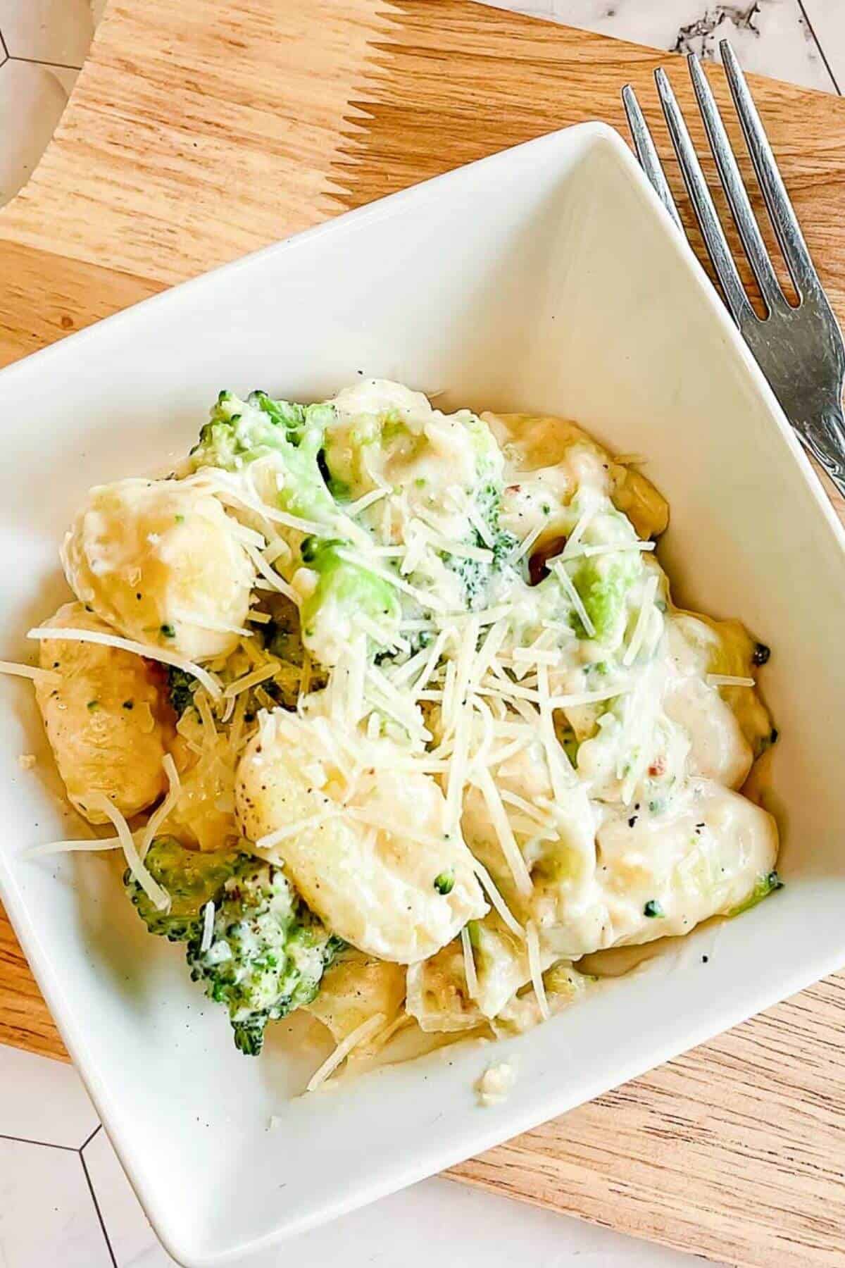 A square white bowl with creamy gnocchi alfredo with broccoli.