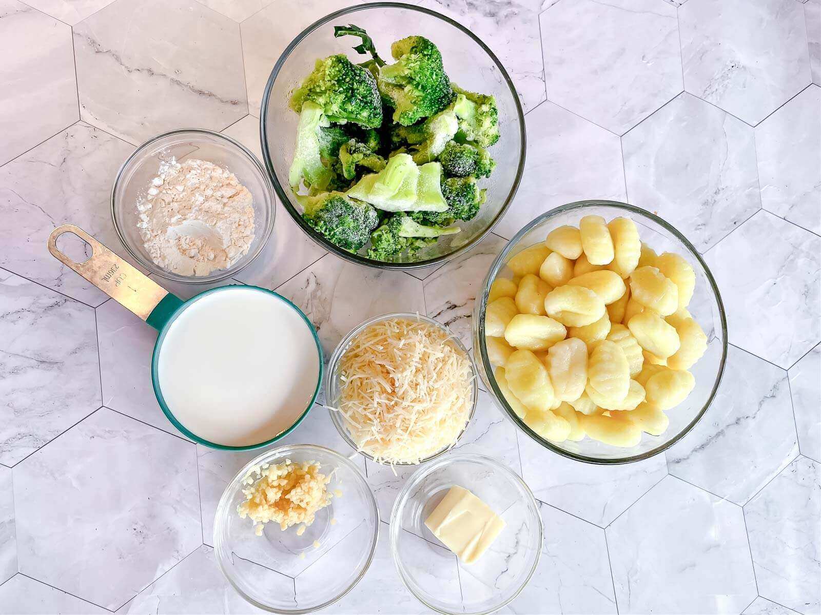 Clear glass bowls of the pasta, vegetables, cream and cheese.
