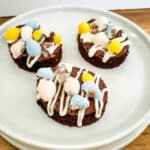 Three chocolate easter brownies topped with pastel Easter candies and white drizzle on a plate.
