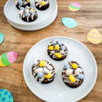 A dessert with candy eggs and drizzled icing on a wooden table with Easter-themed paper plates.